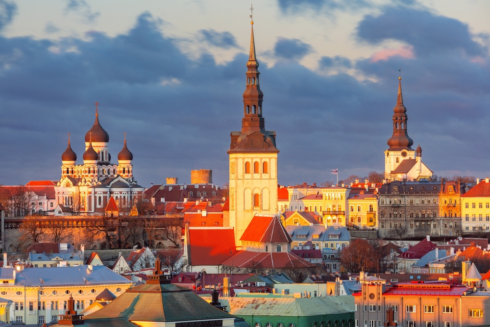 A historic city skyline with church spires and onion domes bathed in the warm light of sunrise or sunset.