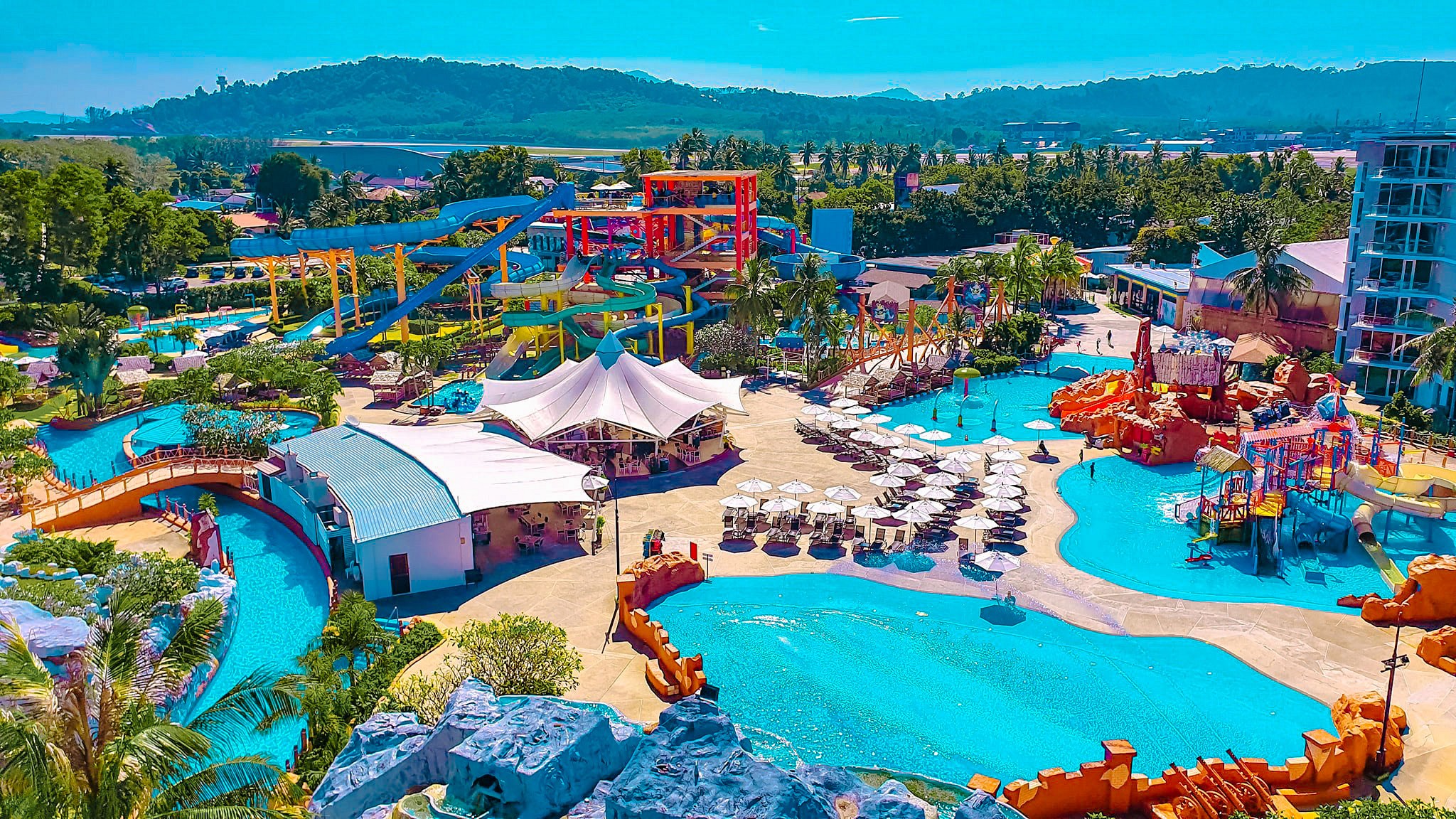 An aerial view of a large, colorful water park with slides and pools on a sunny day.