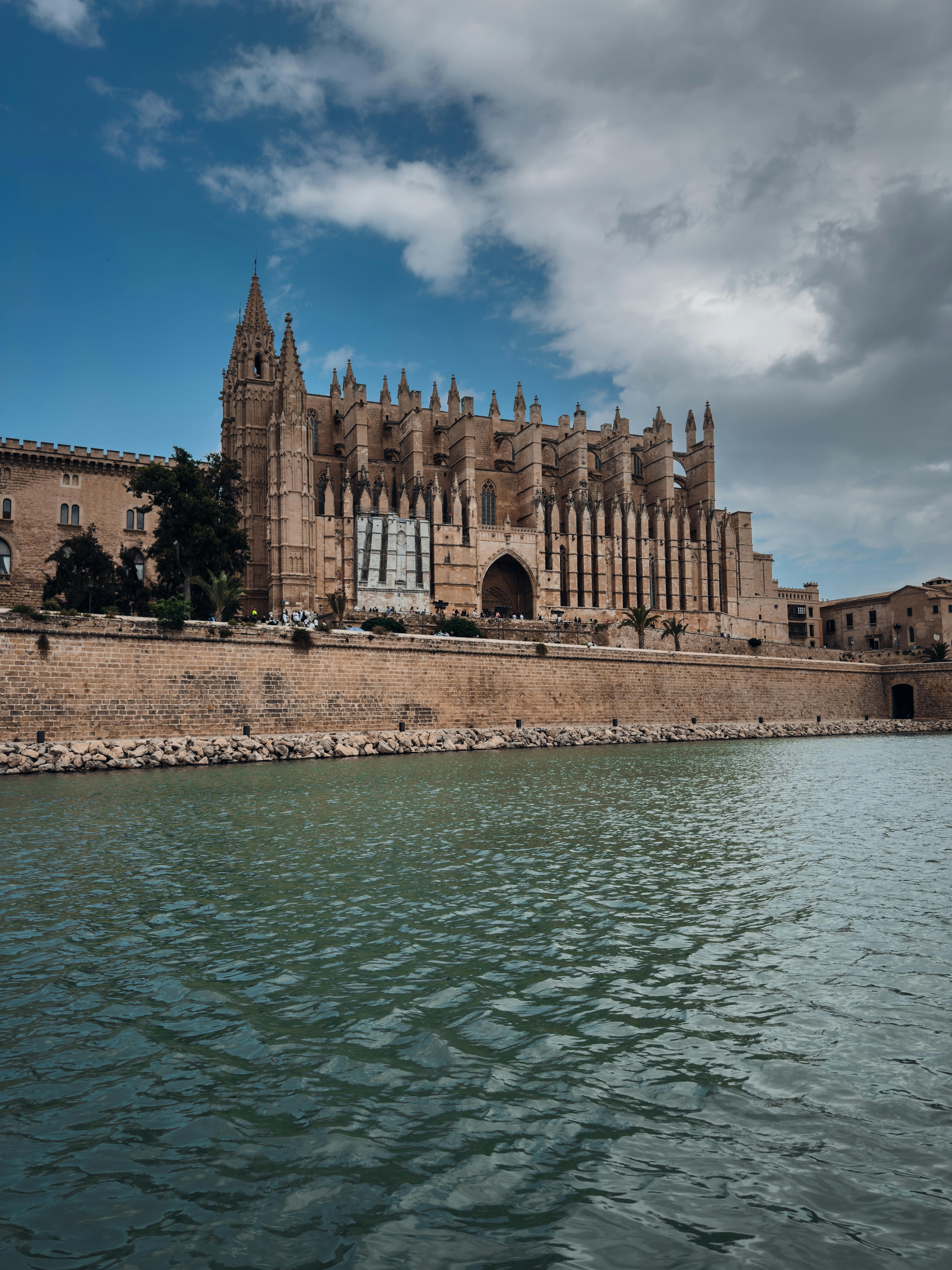 Gothic cathedral by a waterfront under a partly cloudy sky.