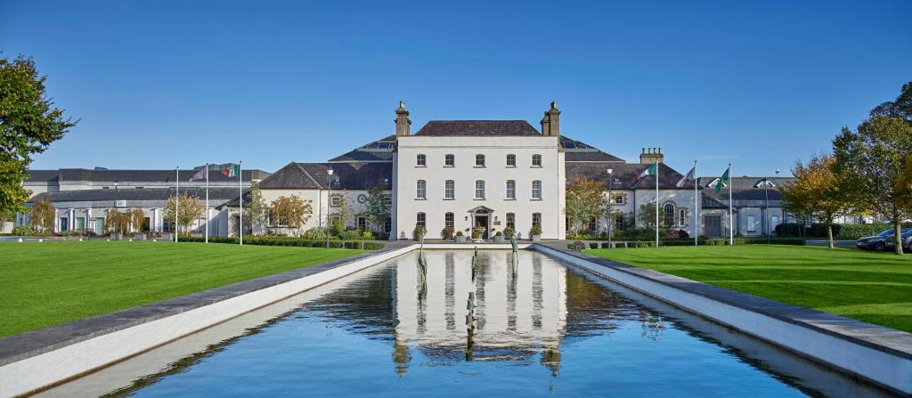 A grand white building with a long reflecting pool on a manicured lawn under a clear blue sky.