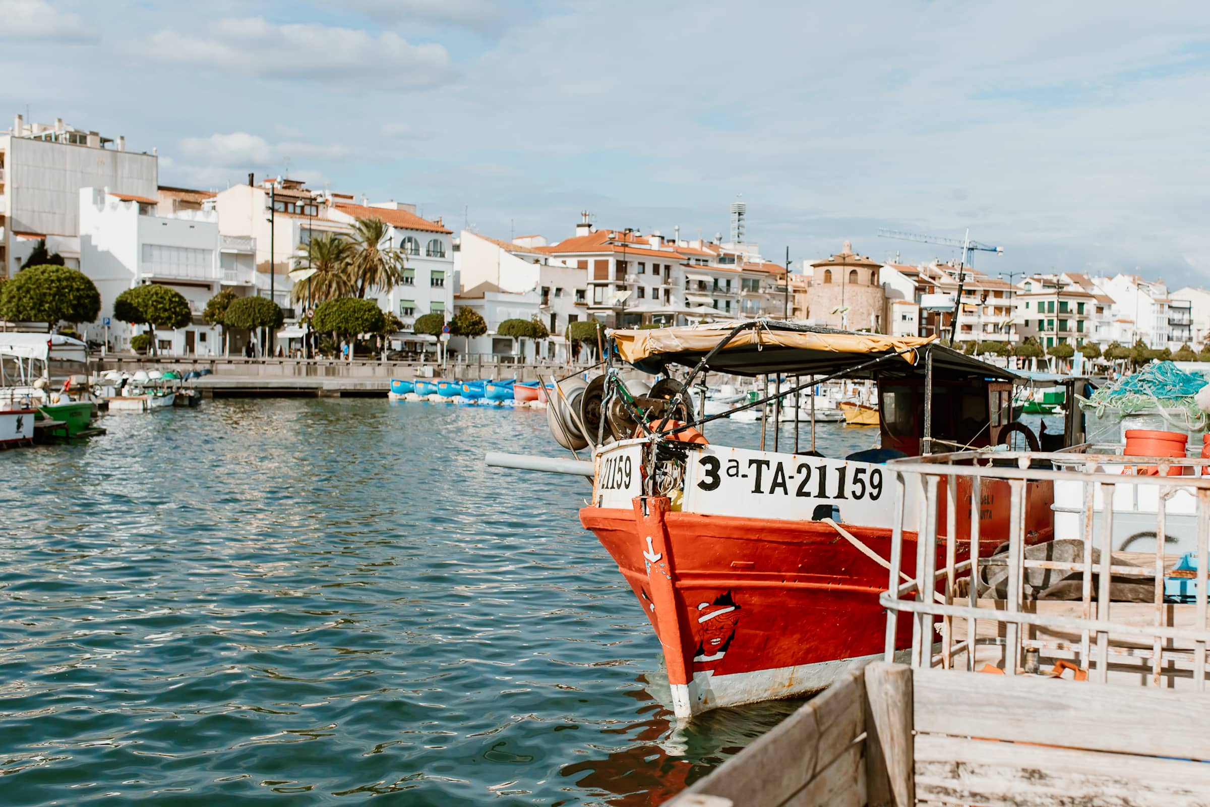Red fishing boat docked in a harbor with buildings in the background.