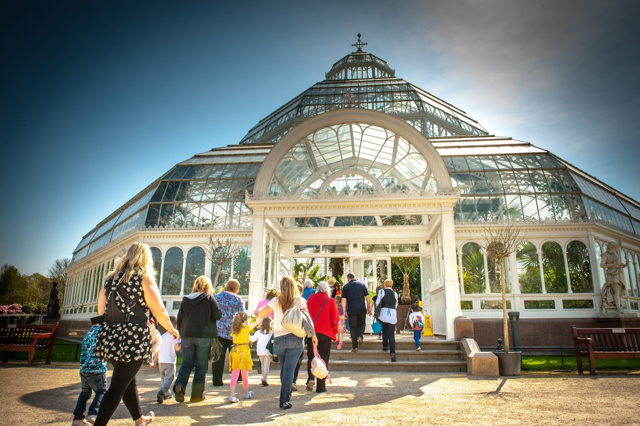 People entering a large glass conservatory on a sunny day.