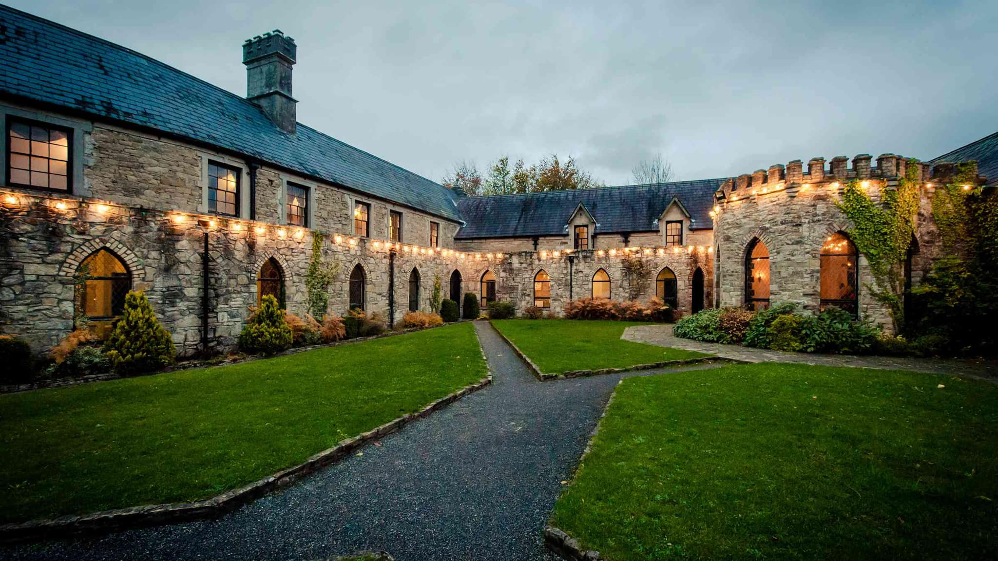 Stone courtyard with arched windows, string lights, and green lawn.