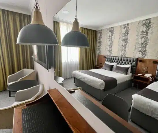 Modern hotel room with double bed, chairs, desk, and decorative wallpaper.