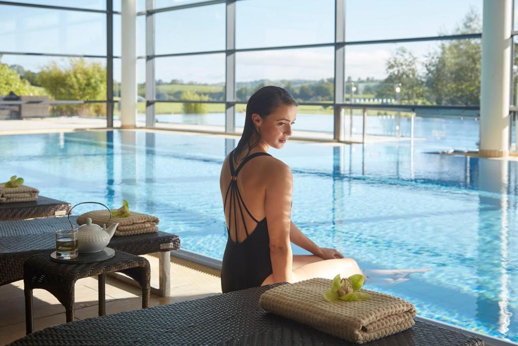 Woman in swimsuit sitting by indoor pool with tea set on table.
