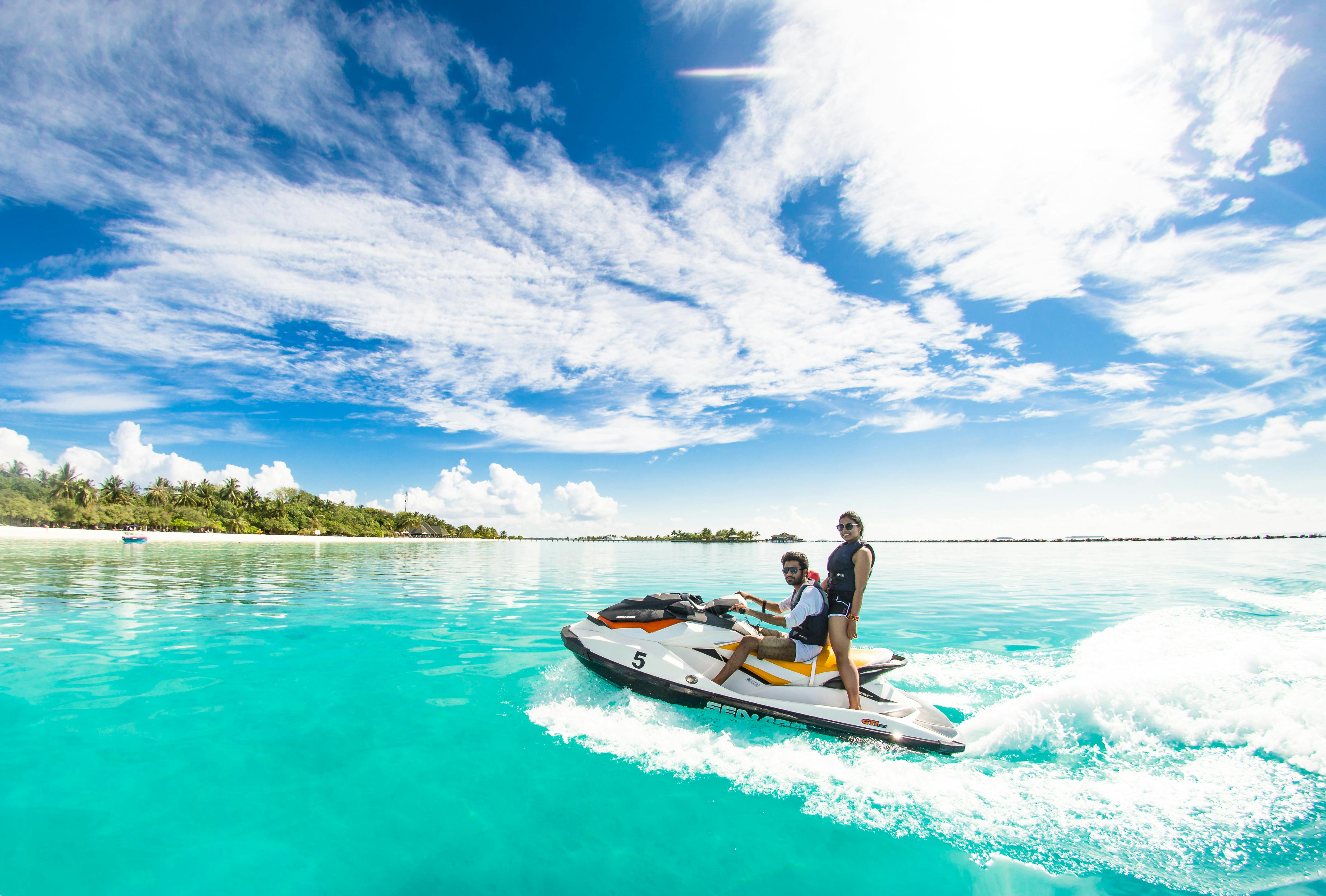 Two people riding a jet ski on clear turquoise water under a blue sky.