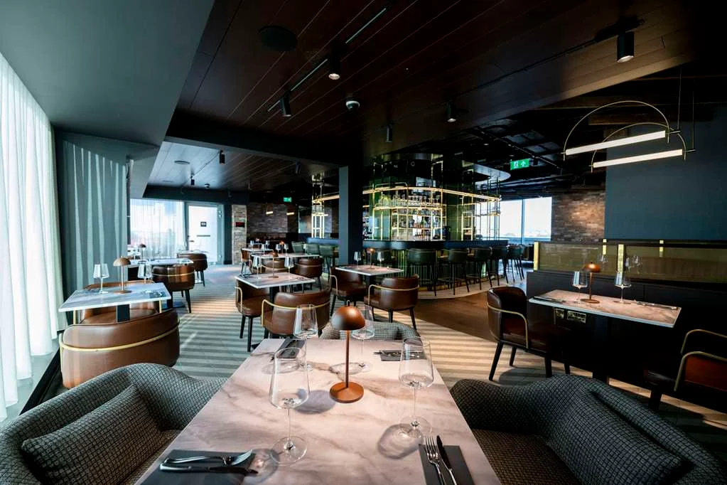 Modern restaurant interior with elegant tables, chairs, and a central bar area.