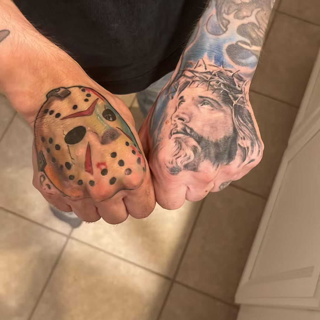 Two hands with tattoos: a hockey mask and a crowned figure.