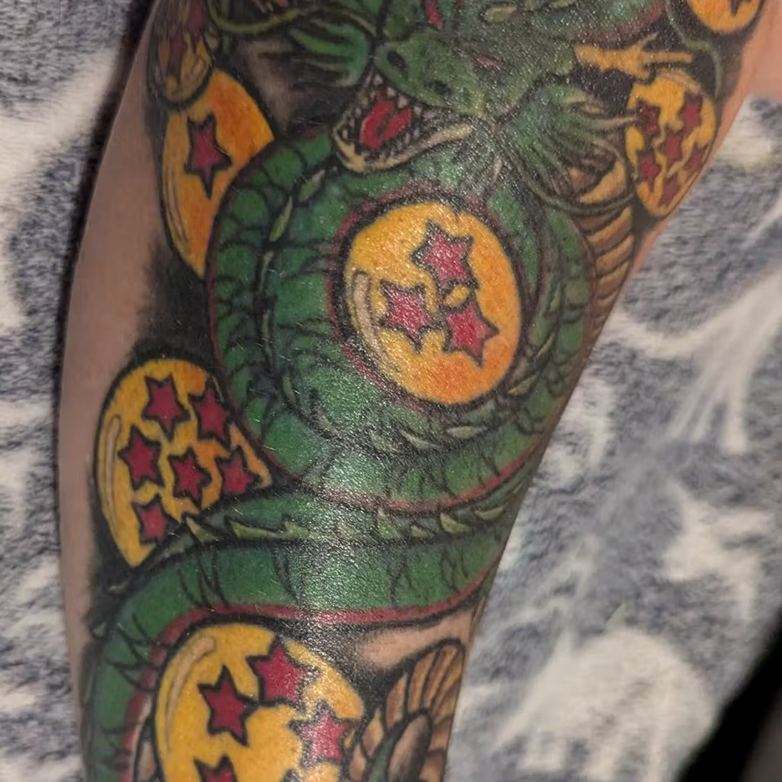 Tattoo of a green dragon and yellow spheres with red stars on an arm.