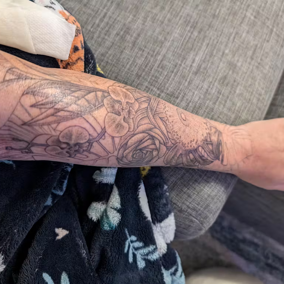 Forearm with detailed floral and leaf tattoo design.