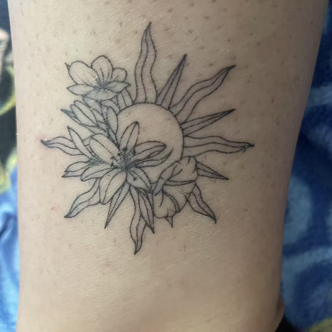 Tattoo of a sun and flowers on skin.