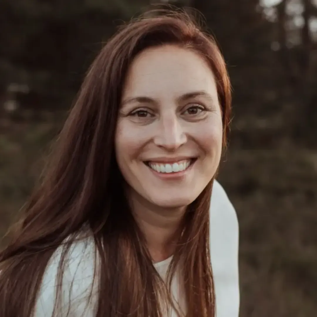 A headshot of a smiling woman with long brown hair outdoors.