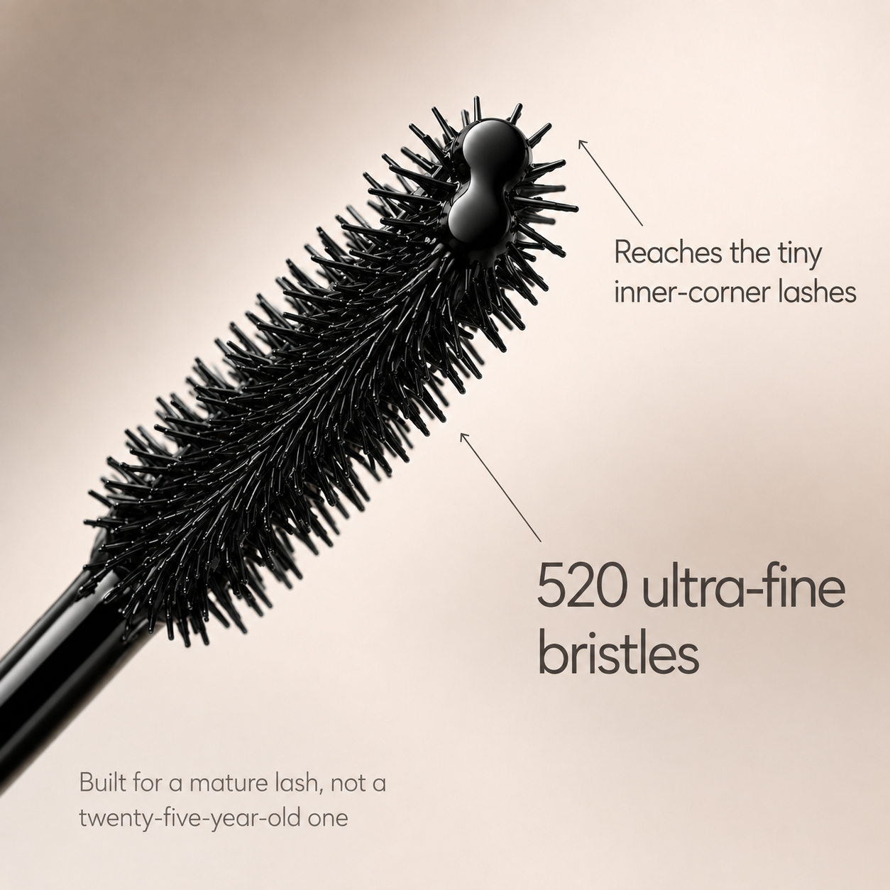 A close-up of a black mascara wand with text highlighting its features, like its 520 ultra-fine bristles.