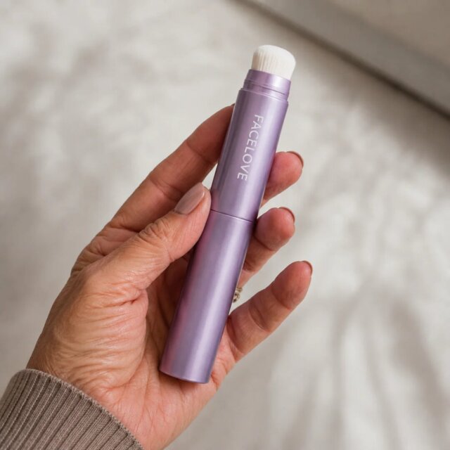 A hand holds a purple, retractable makeup brush with the brand name FACELOVE printed on the side.