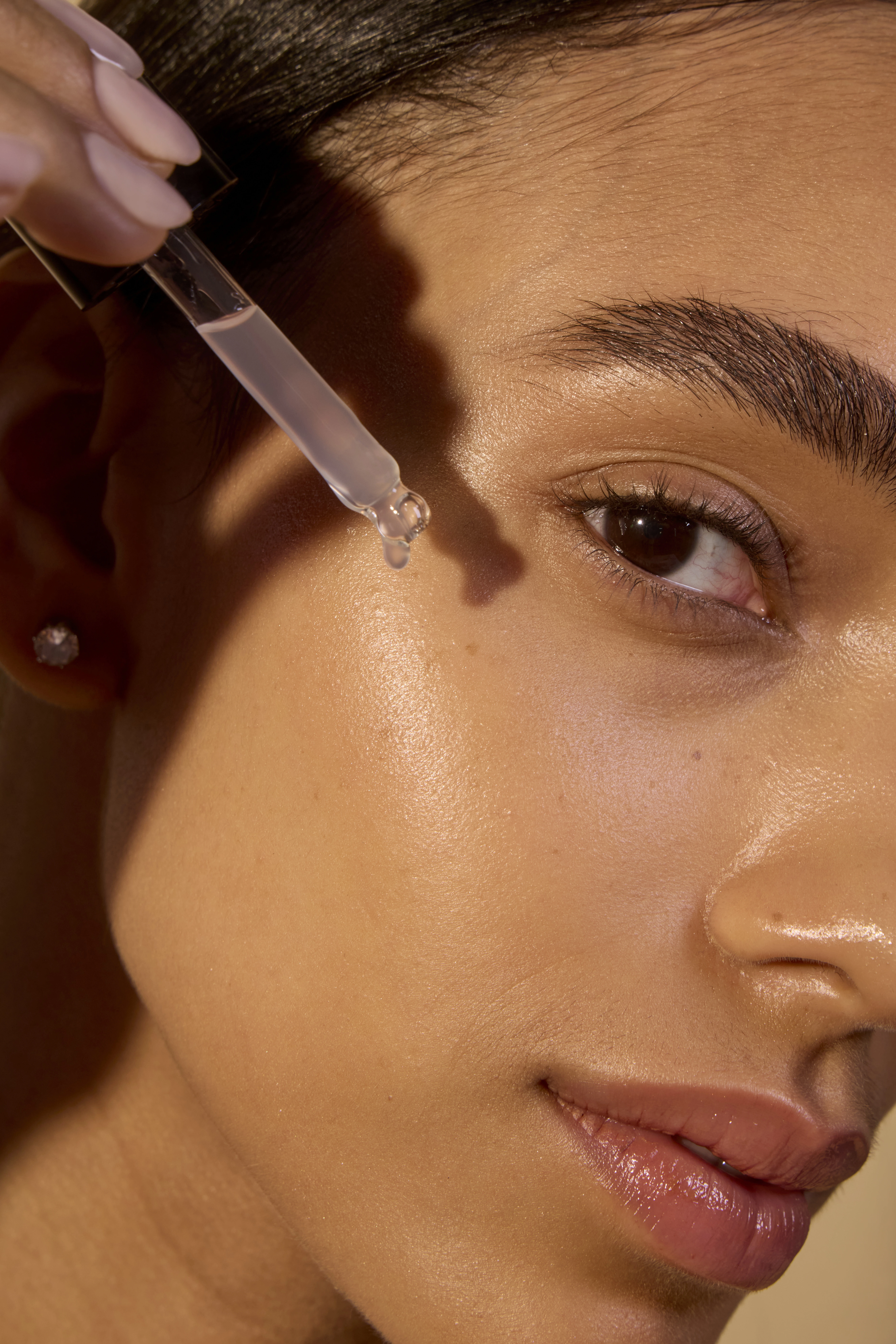 Close-up of a person applying serum with a dropper to their cheek.