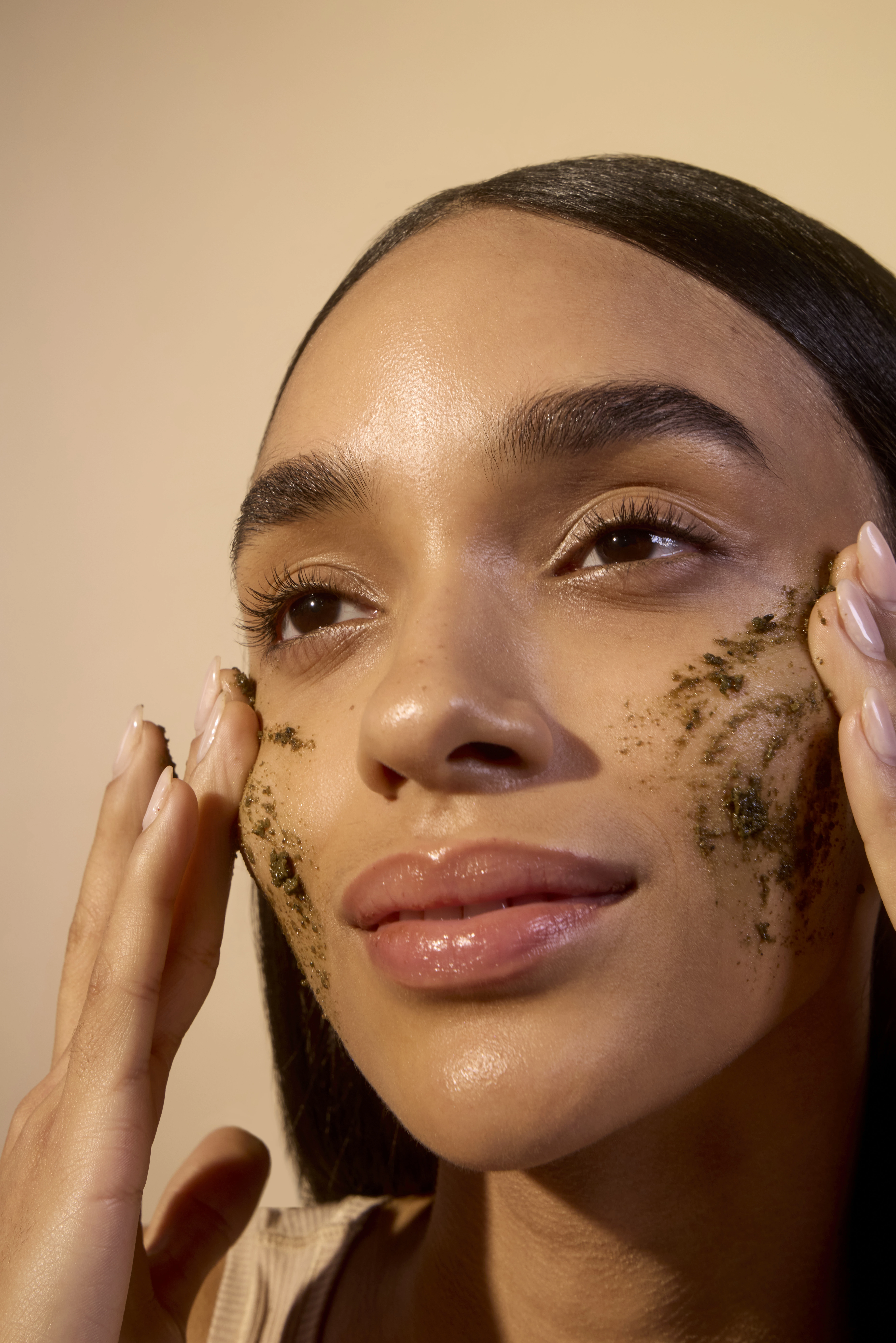 Person applying a facial scrub to their cheeks.