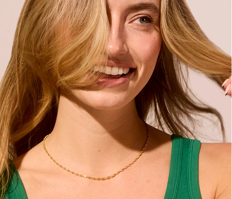 Smiling person with long hair, wearing a green top and gold necklace.