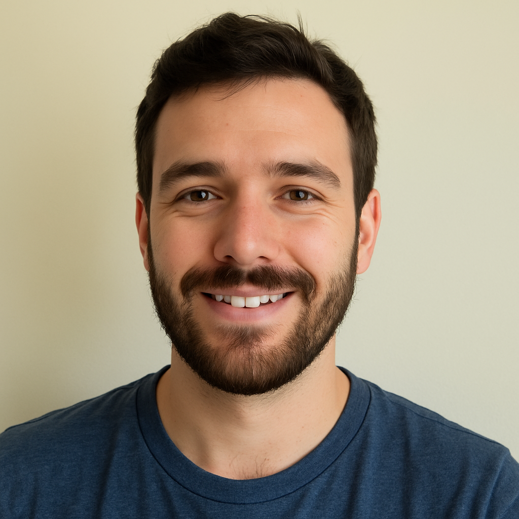Smiling man with a beard wearing a blue shirt against a plain background.
