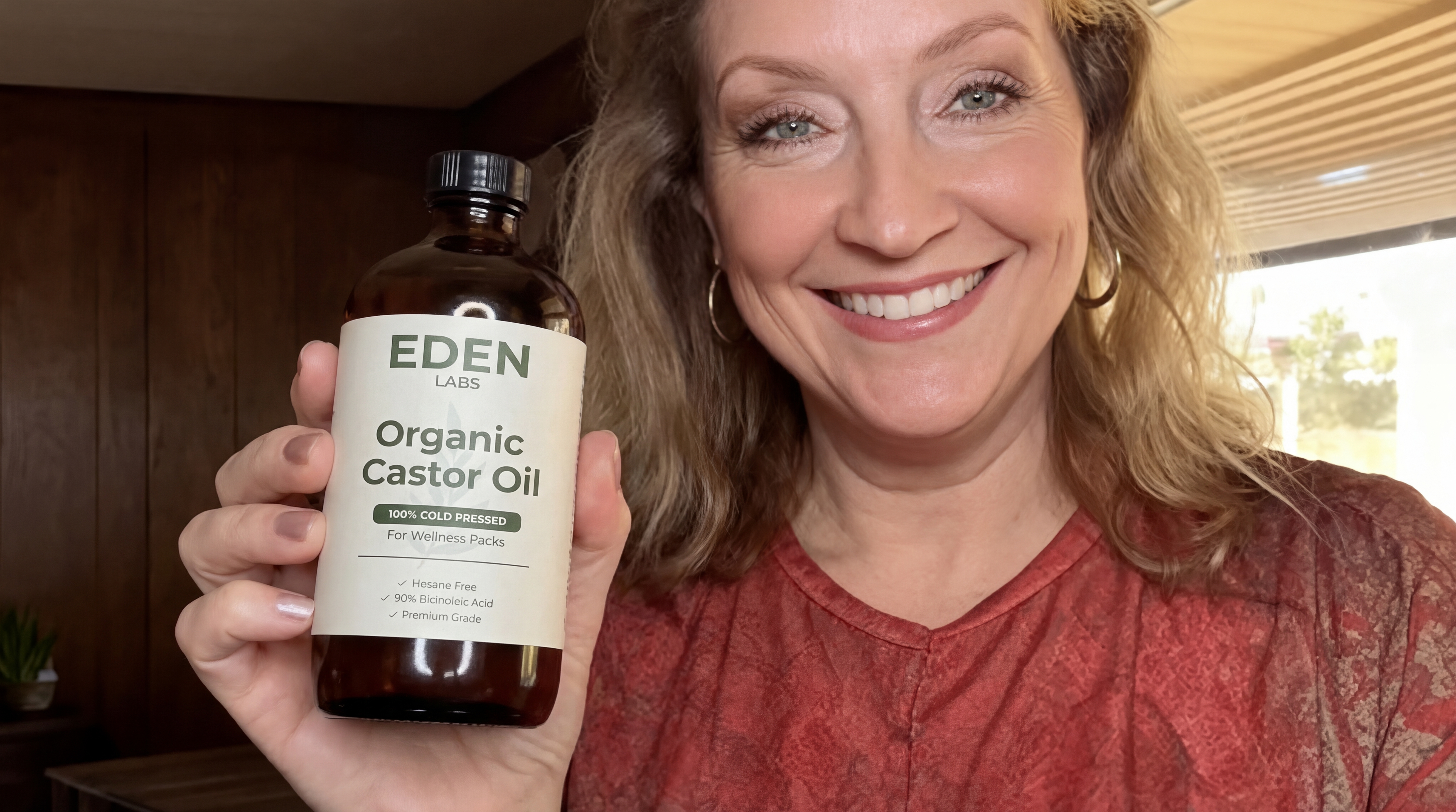 A smiling woman holds up a bottle of Eden Labs Organic Castor Oil.