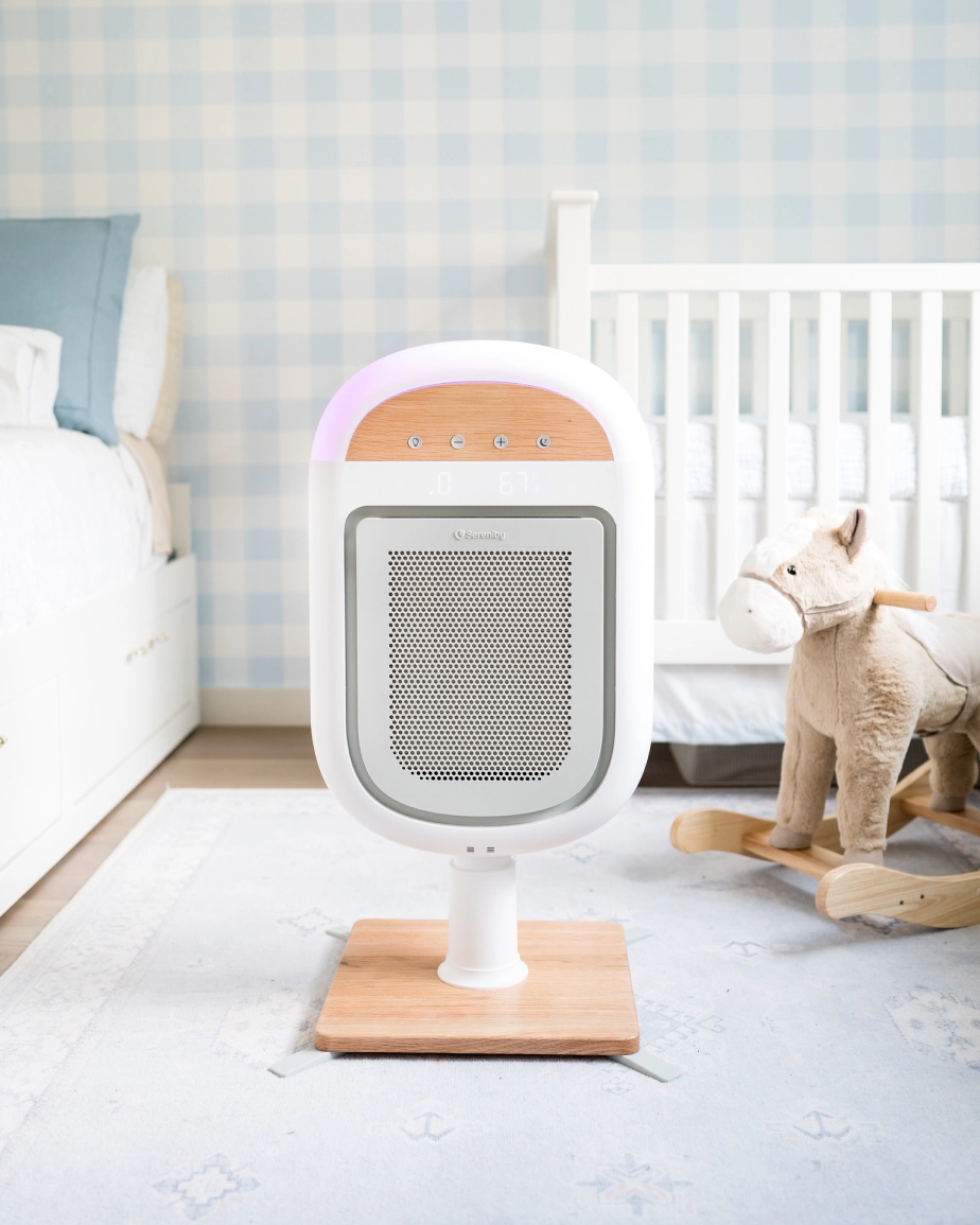 A white and wood air purifier on a stand in a child's bedroom with a crib and rocking horse.