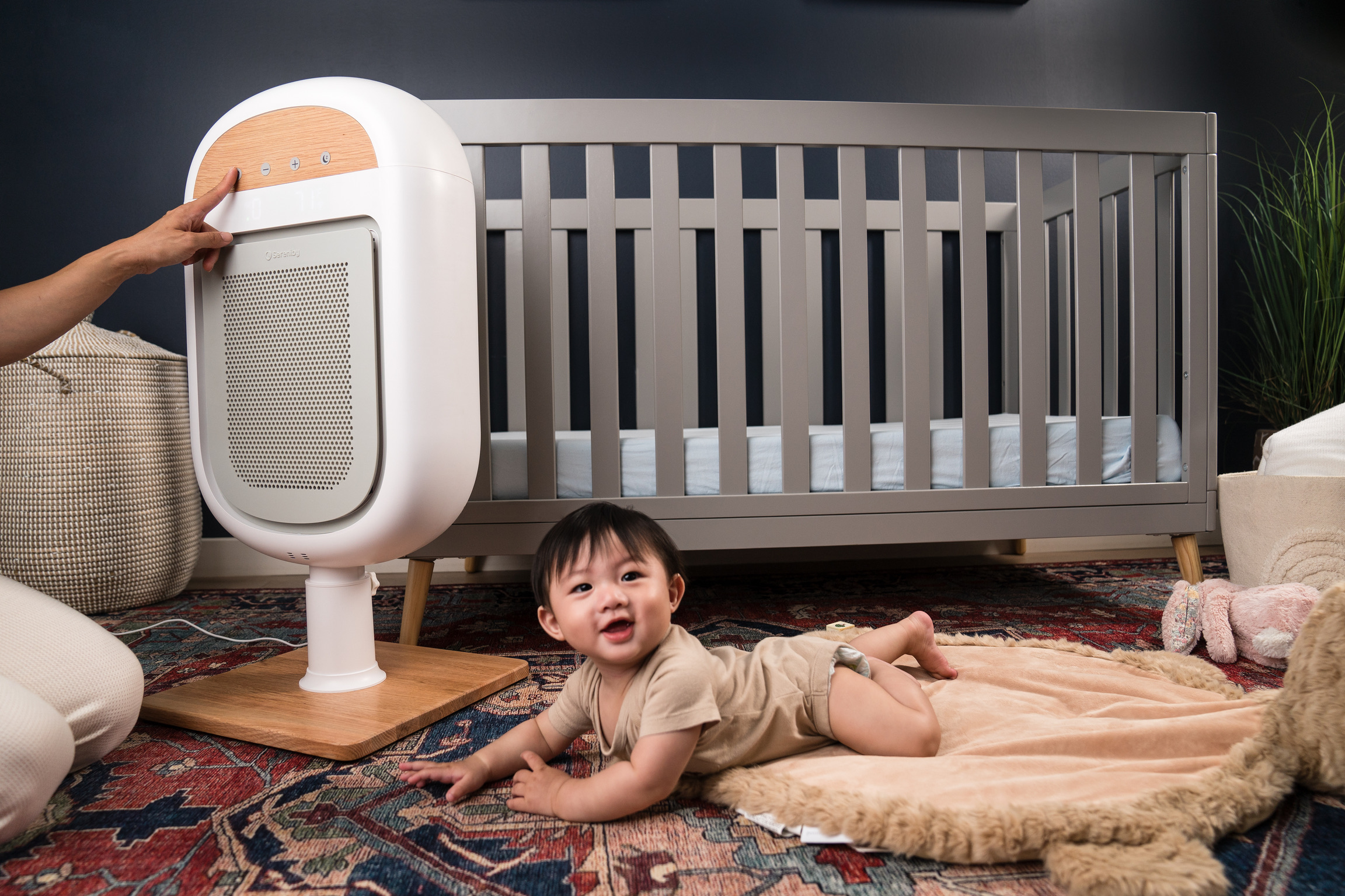 Baby lying on a rug in front of a crib and air purifier.