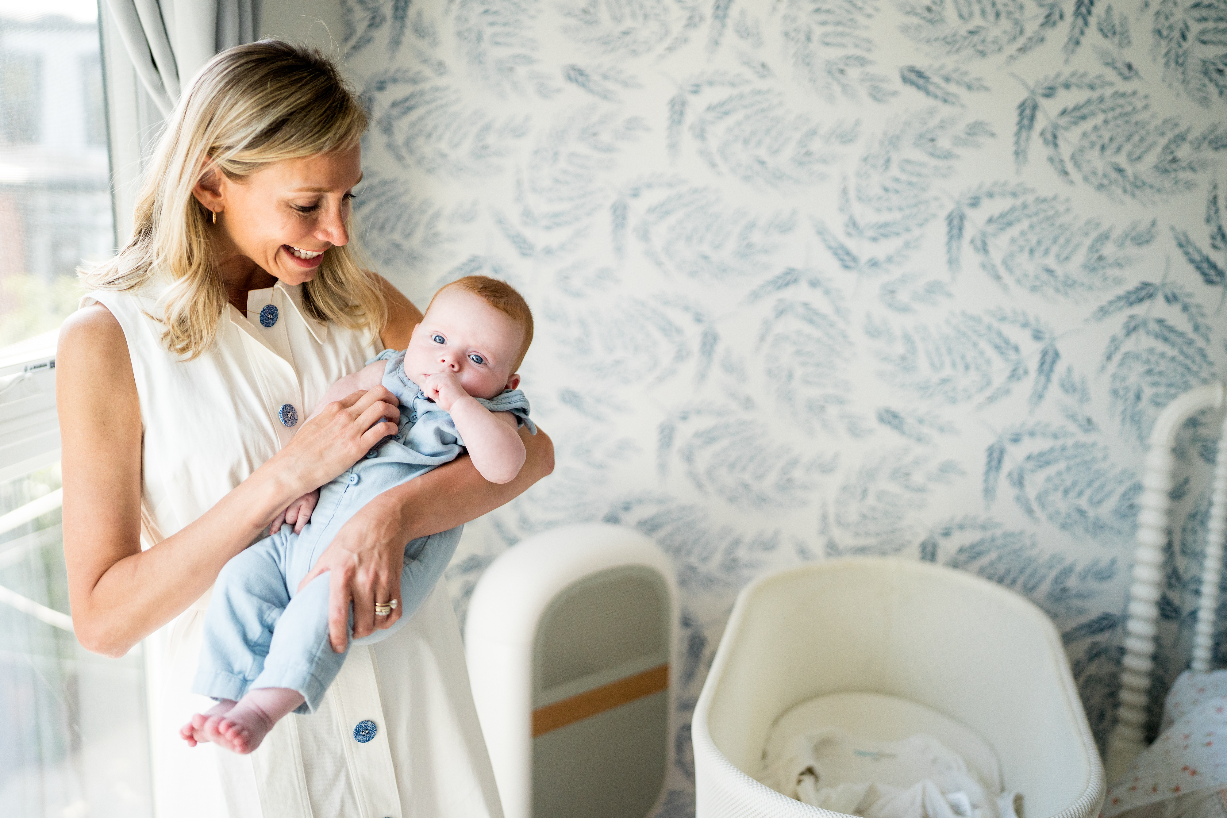Woman holding a baby in a nursery with patterned wallpaper.