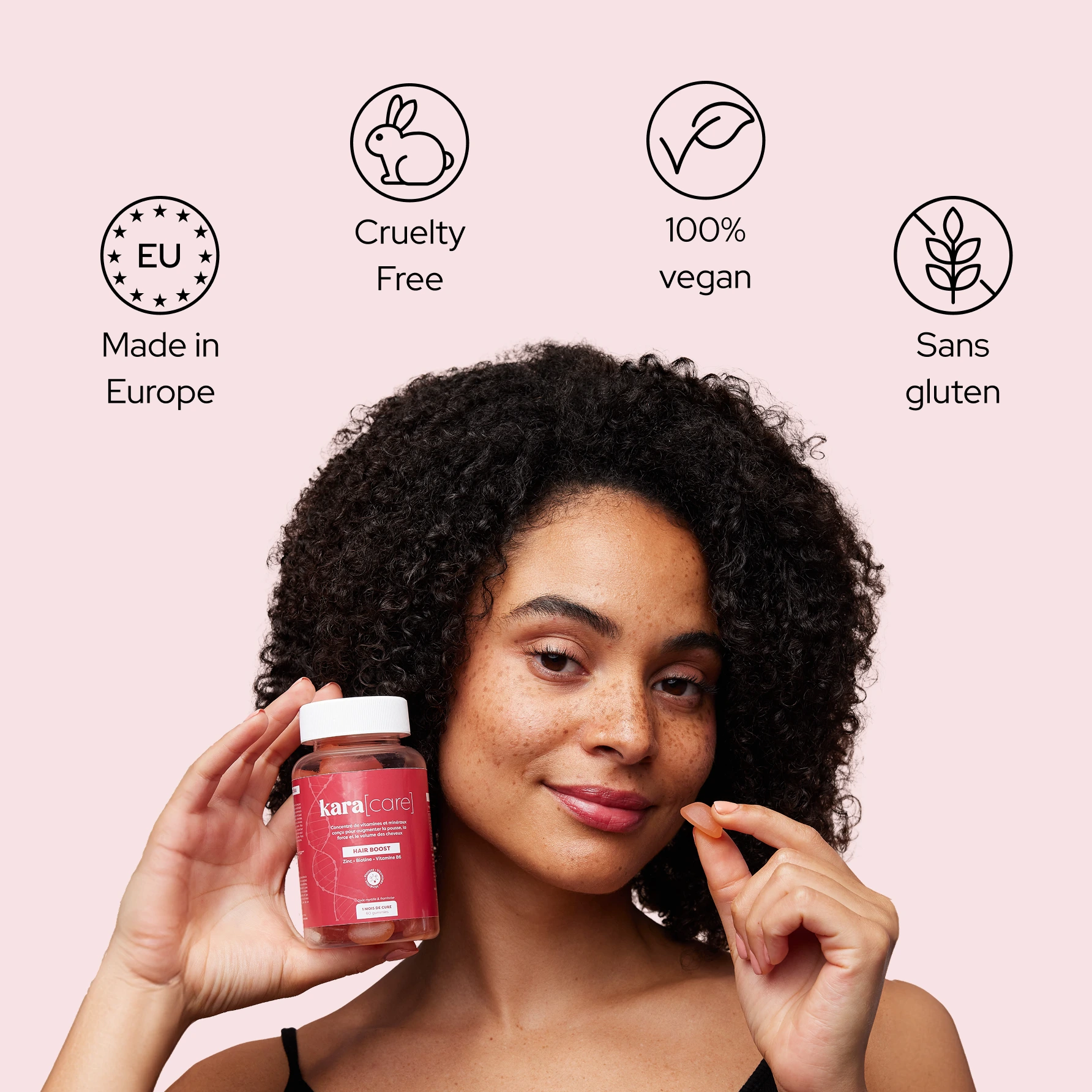 A woman with curly hair holds a bottle of Kara Care gummies and a single gummy, smiling at the camera.