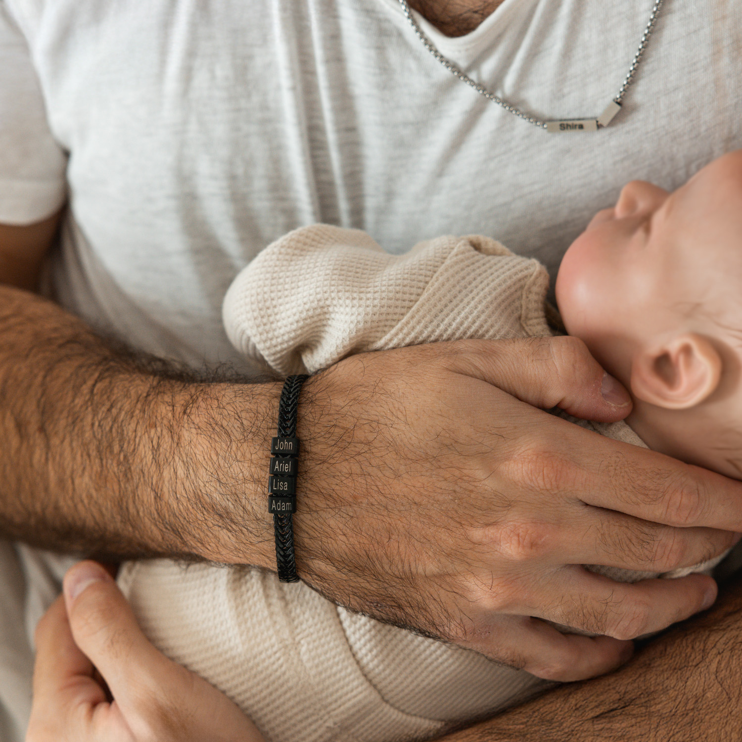 Baby holding an adult's arm wearing a personalized name bracelet.