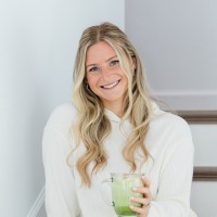 Person smiling, holding a green beverage, sitting on stairs.