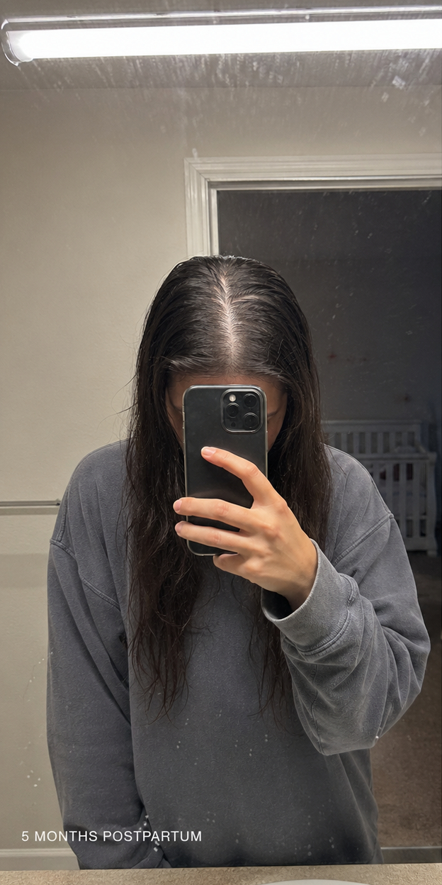 A person with long, wet, dark hair parted in the middle takes a selfie in a mirror.