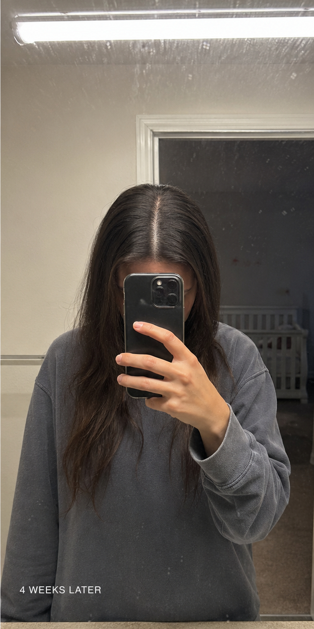A person with long dark hair takes a selfie in a mirror, obscuring their face with a phone.