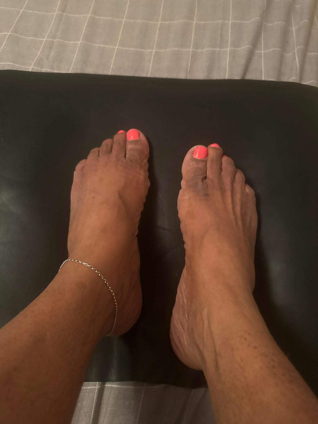 Feet with pink toenails and an ankle bracelet on a black and gray background.