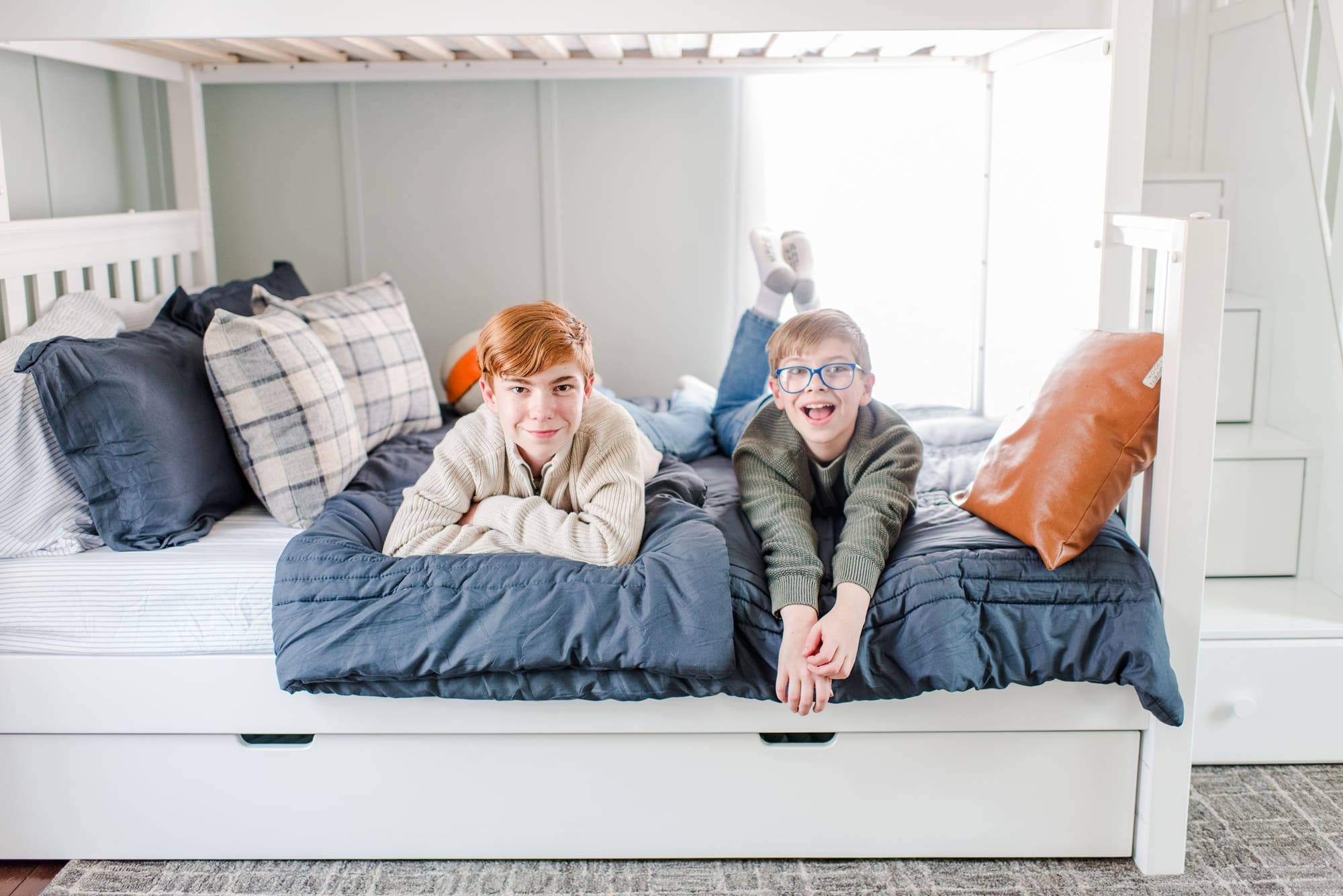 Two boys smiling and relaxing on a bunk bed in a cozy bedroom setting.