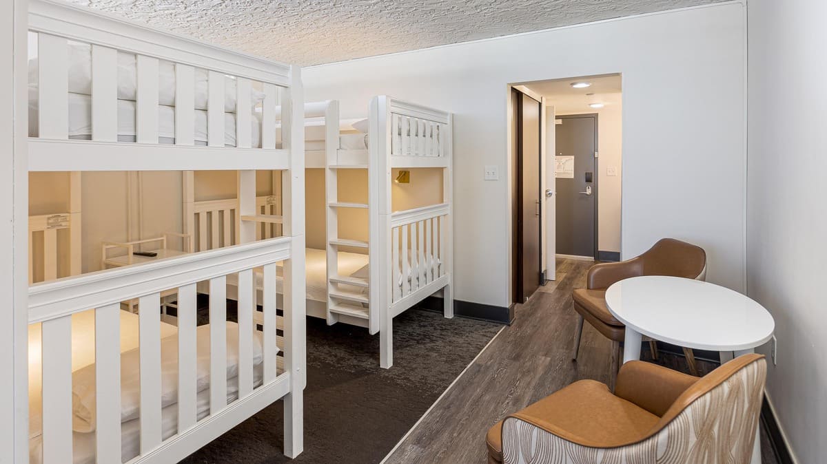 Room with two sets of white bunk beds, chairs, and a small table.