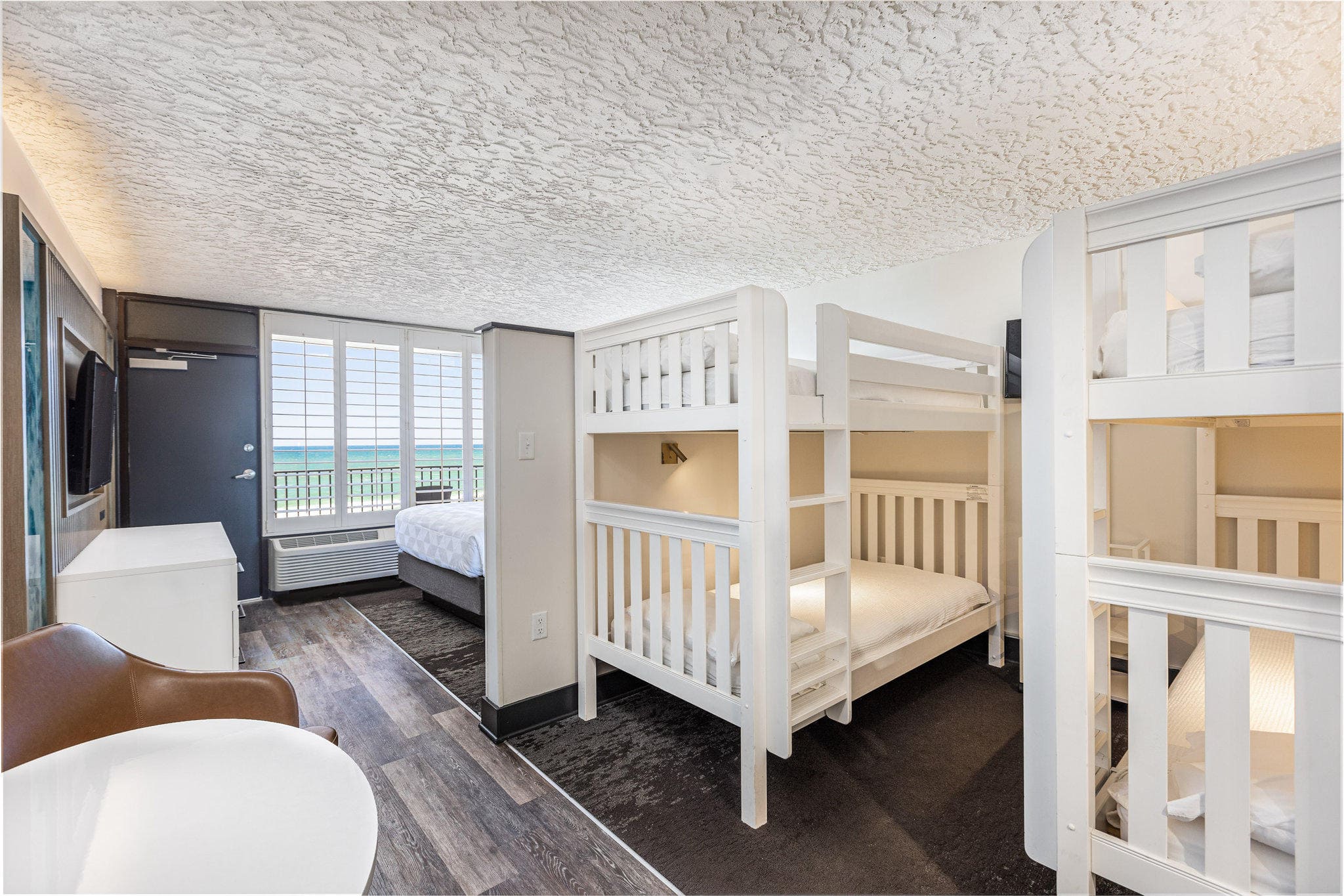 Room with bunk beds, a double bed, and ocean view through large windows.