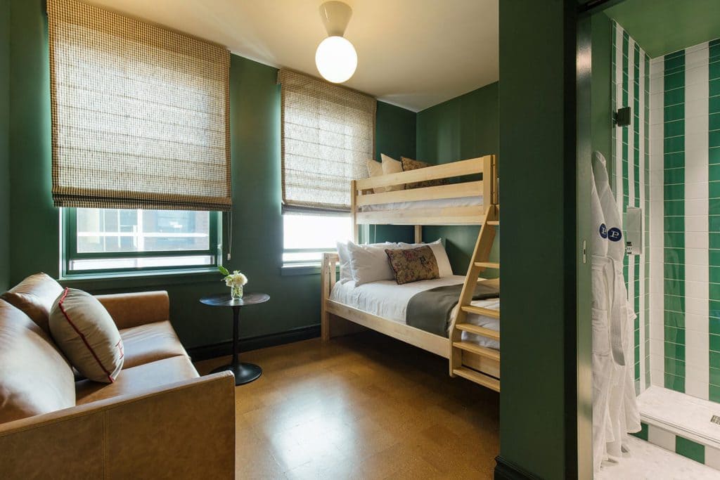 Room with bunk bed, sofa, table, and bathroom with green tiles.
