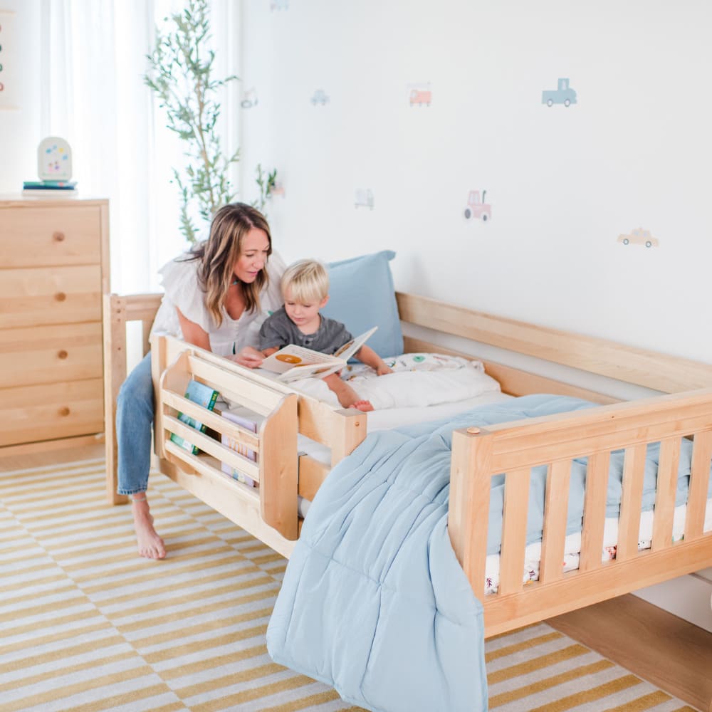 Woman reading a book with her son in wooden toddler bed.