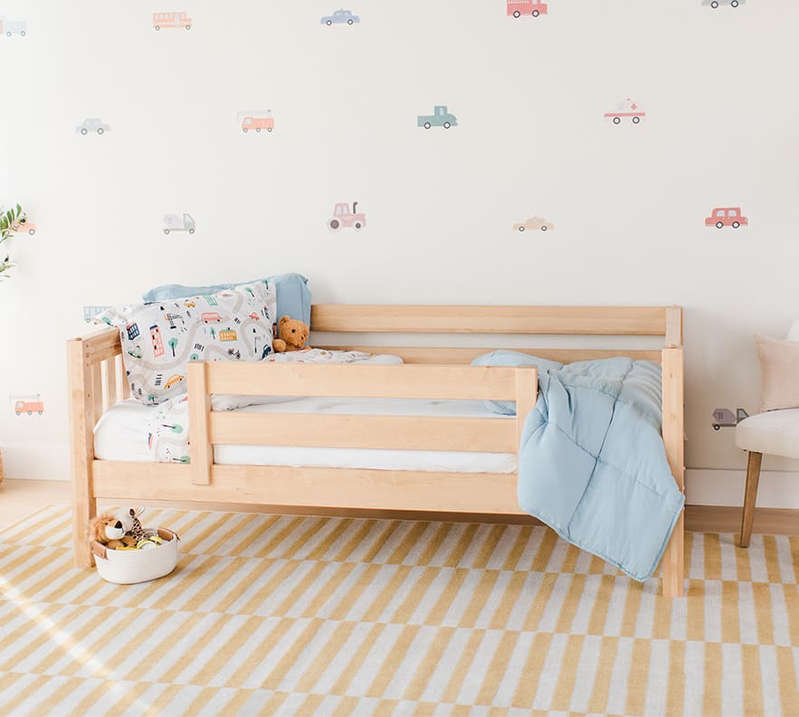 Toddler bed with blue bedding and colorful vehicle wall decals in a cozy children's room.