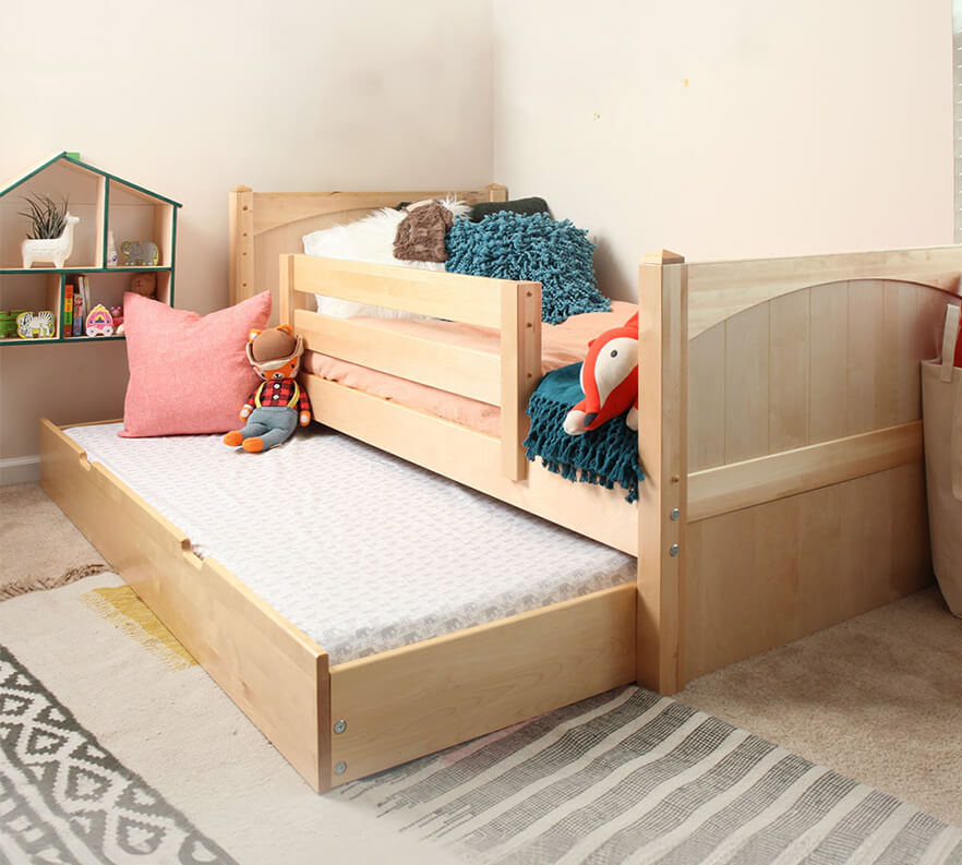 Wooden toddler bed with pull-out trundle in cozy bedroom setting with plush toys and decorative pillows.