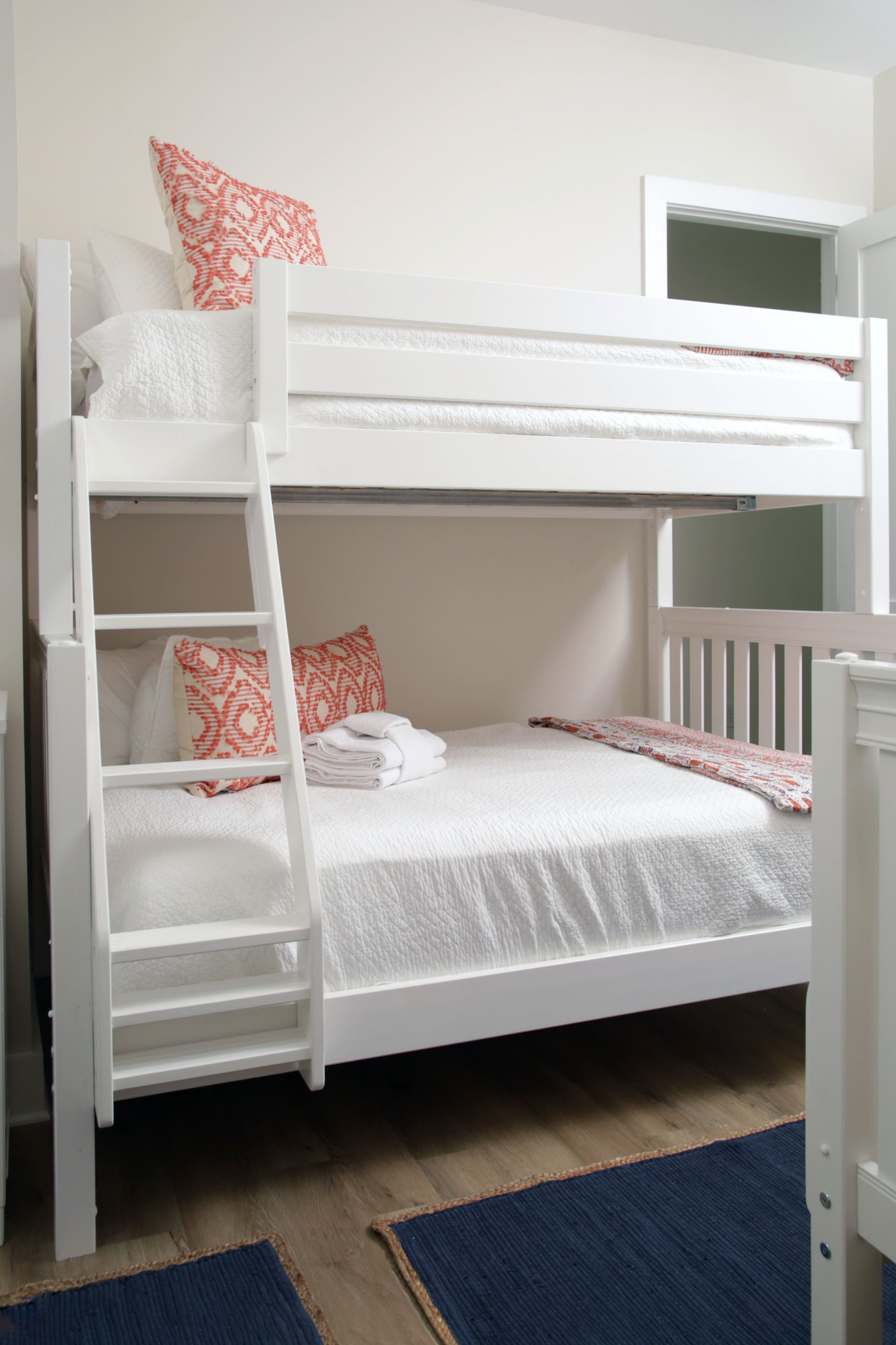 White bunk bed with orange patterned pillows and folded towels.