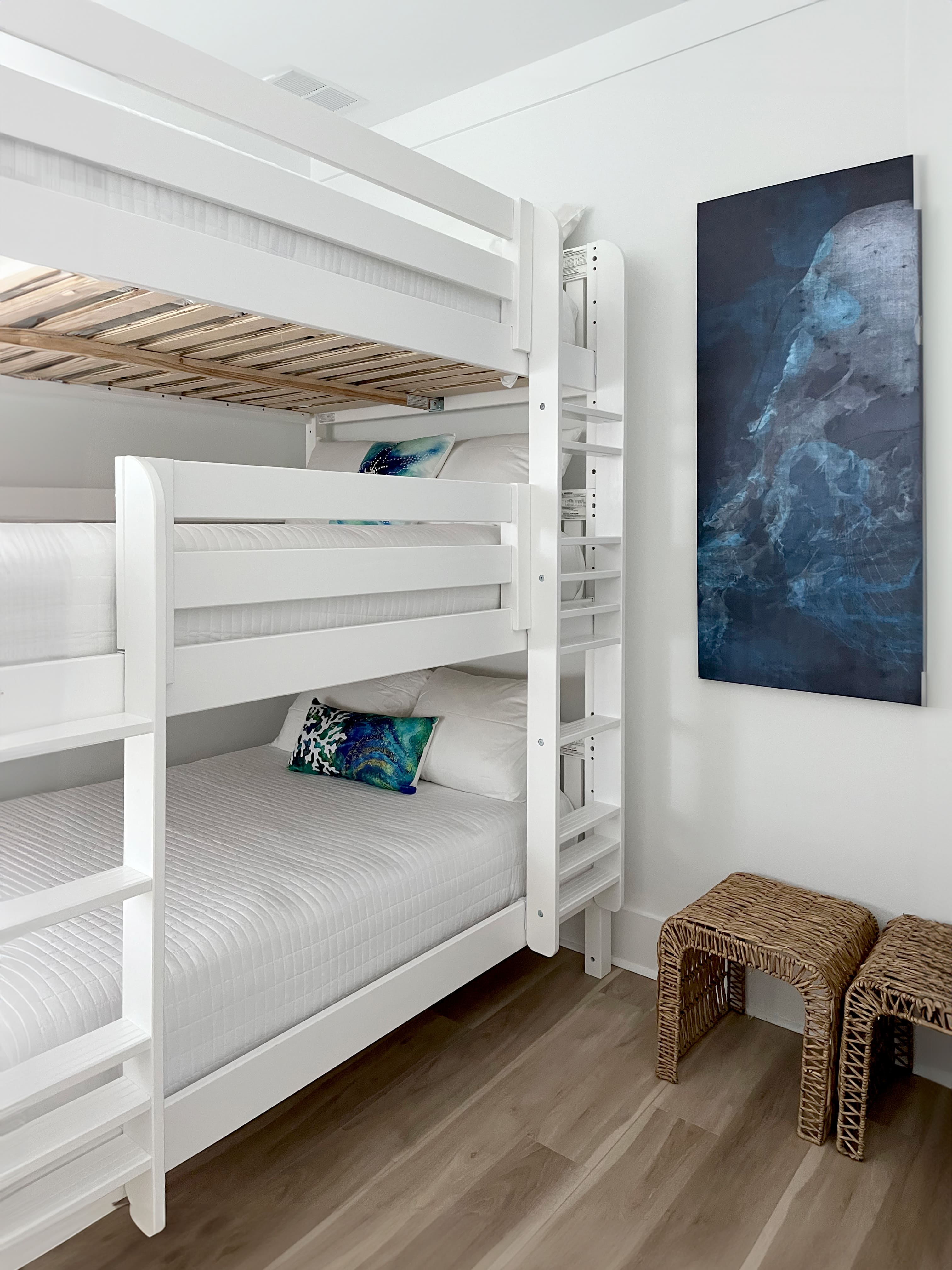 White bunk beds with decorative pillows and a blue abstract painting on the wall.