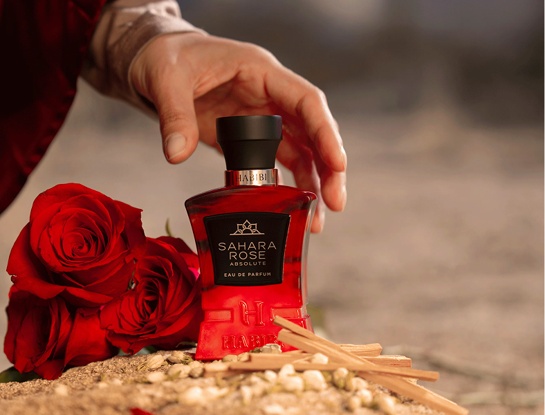 Red perfume bottle with roses and a hand reaching for it.