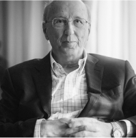 A black-and-white portrait of an older man in a suit and glasses.