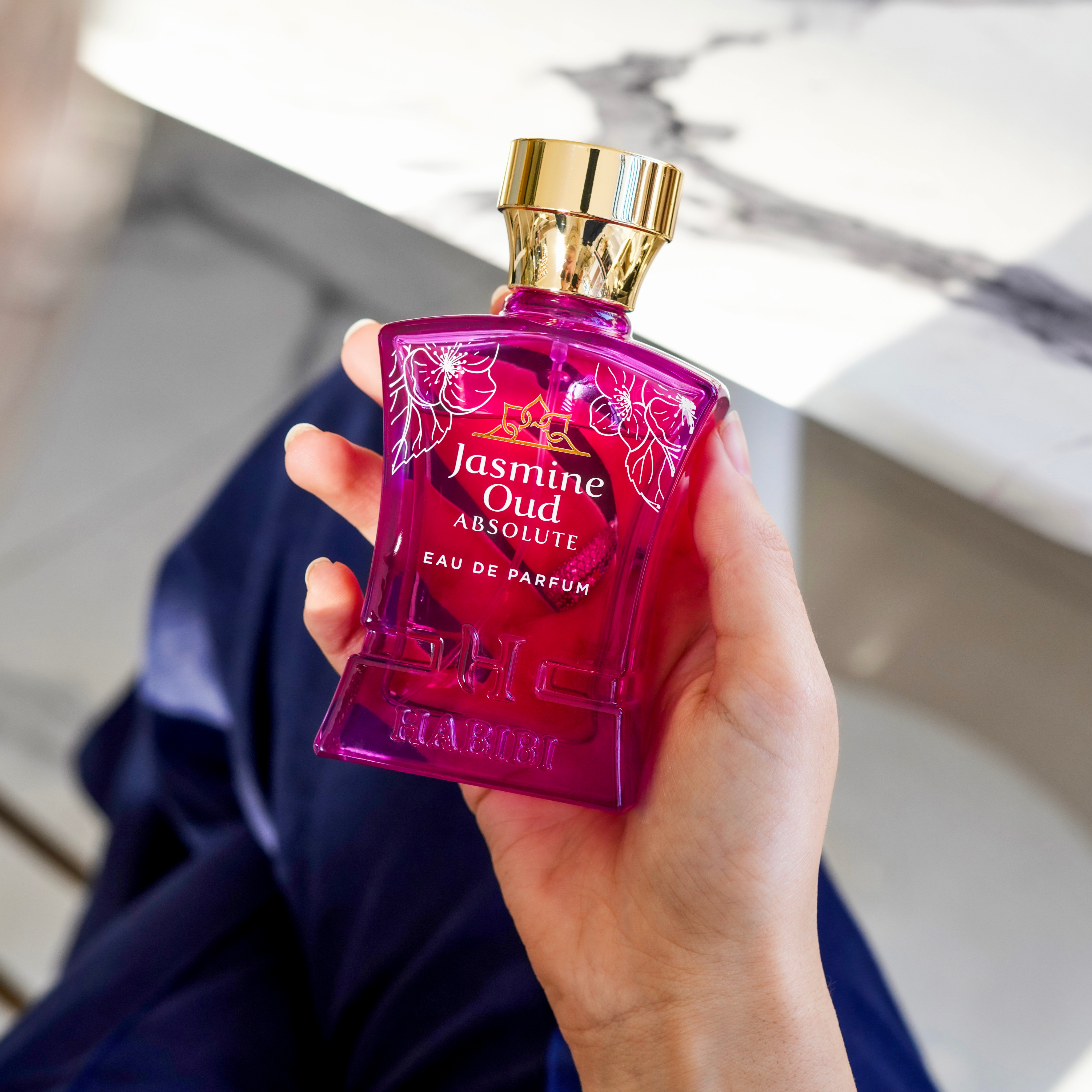 Hand holding a purple perfume bottle labeled 'Jasmine Oud Absolute.'