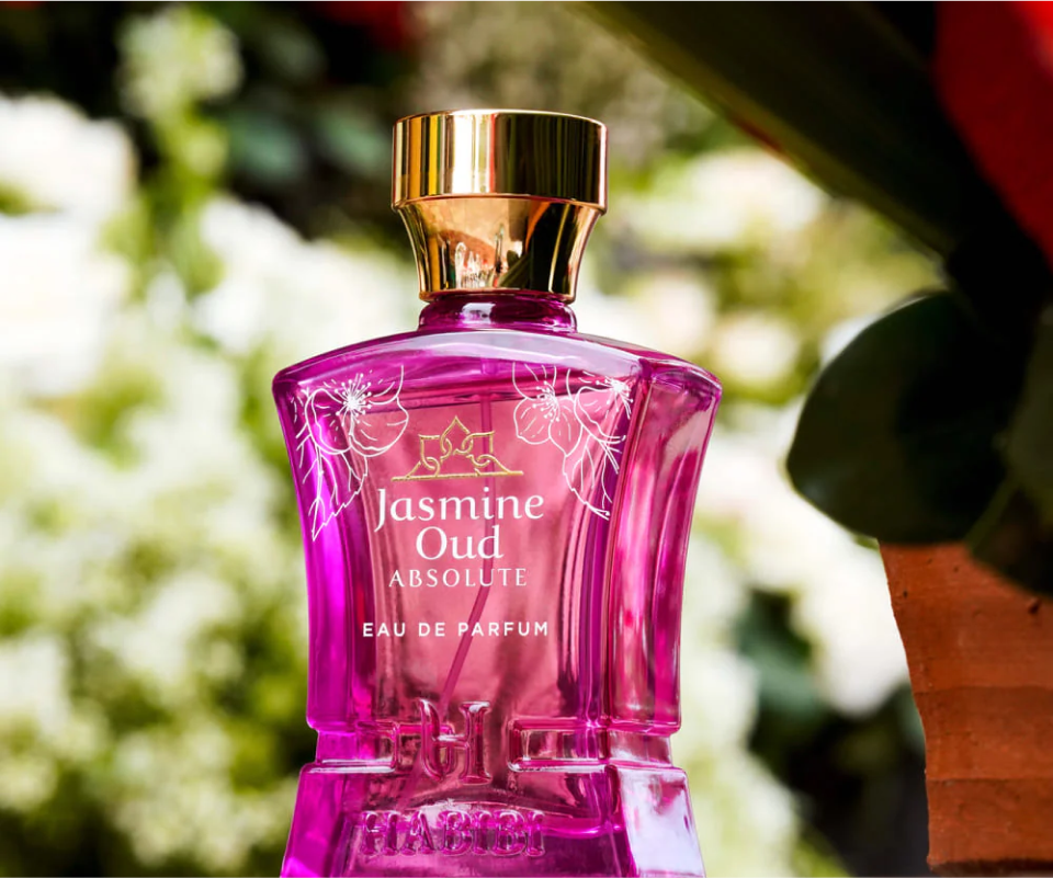 Pink perfume bottle labeled 'Jasmine Oud Absolute' with floral design, outdoors.