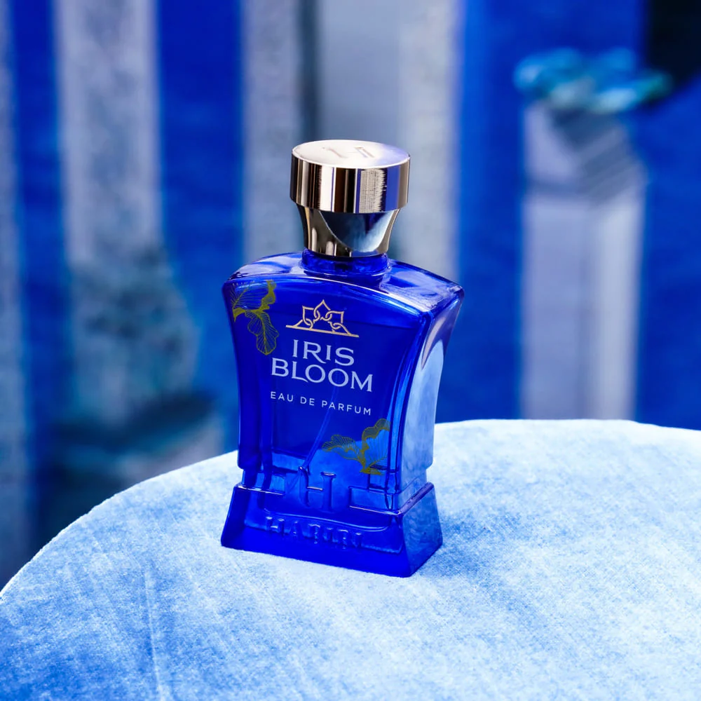 Blue perfume bottle labeled 'Iris Bloom' on a blue surface.