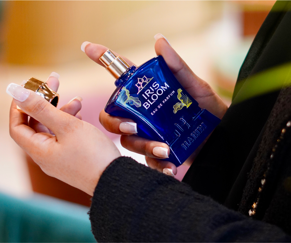 Person holding a blue perfume bottle labeled 'Iris Bloom' with a gold cap.