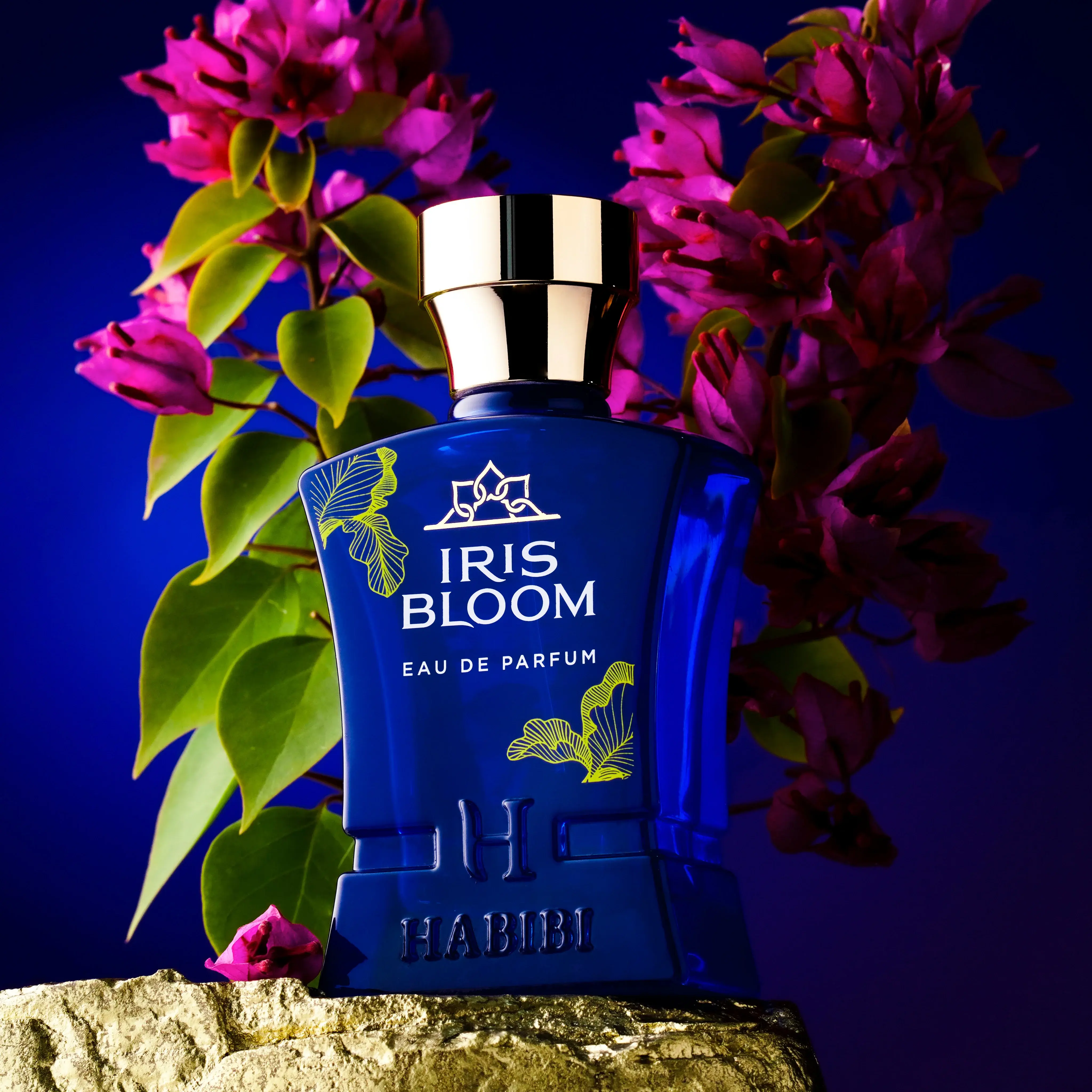 Blue perfume bottle with gold cap, surrounded by pink flowers and green leaves.