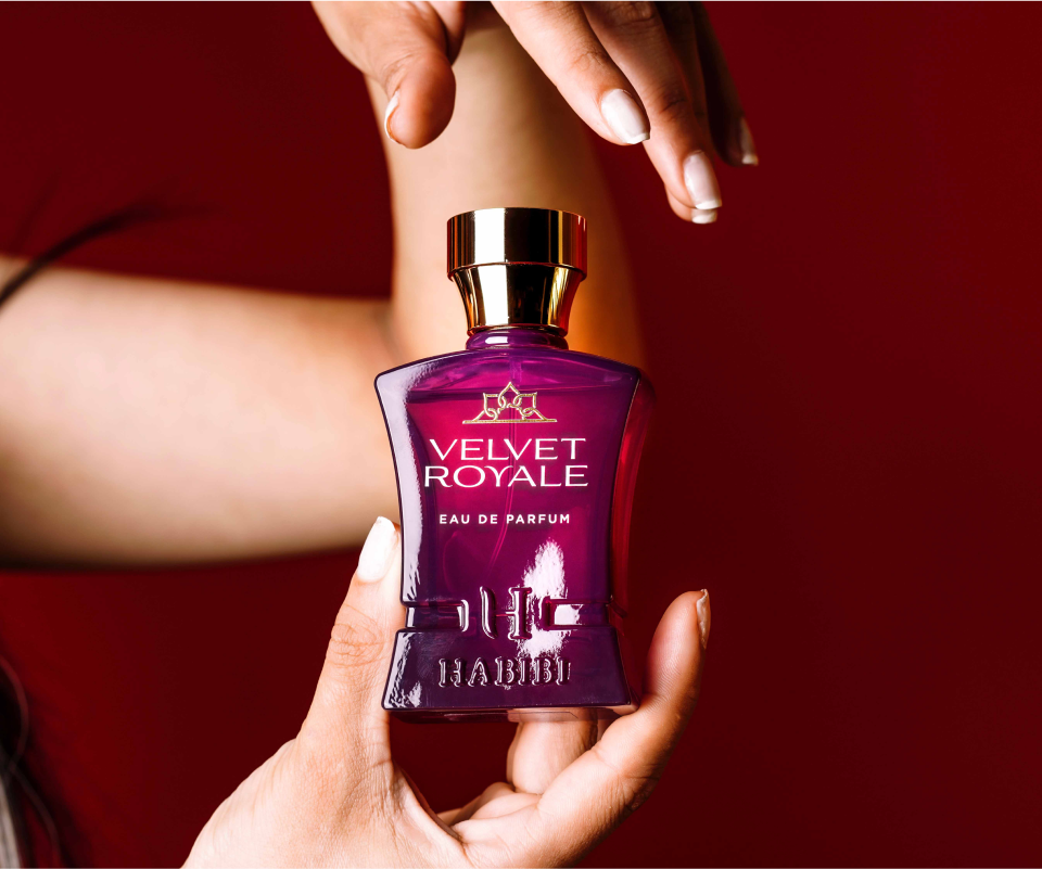 Hands holding a purple perfume bottle labeled 'Velvet Royale' against a red background.