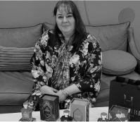 Woman sitting on a couch with perfume bottles on a table in front of her.